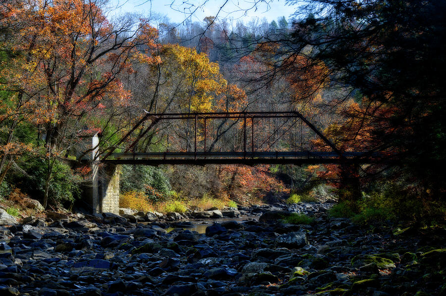 A rustic iron bridge spans over a rocky riverbed by Dan Friend